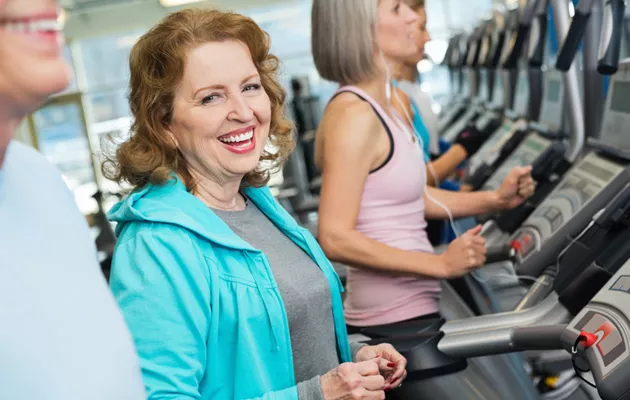 Varttunut nainen hymyilee kuntoillessaan juoksumatolla, osteoporoosin ehkäisy