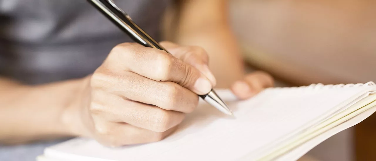 Kirjoittamisterapia voi auttaa kriisissä, nainen kirjoittaa kynällä paperille.
