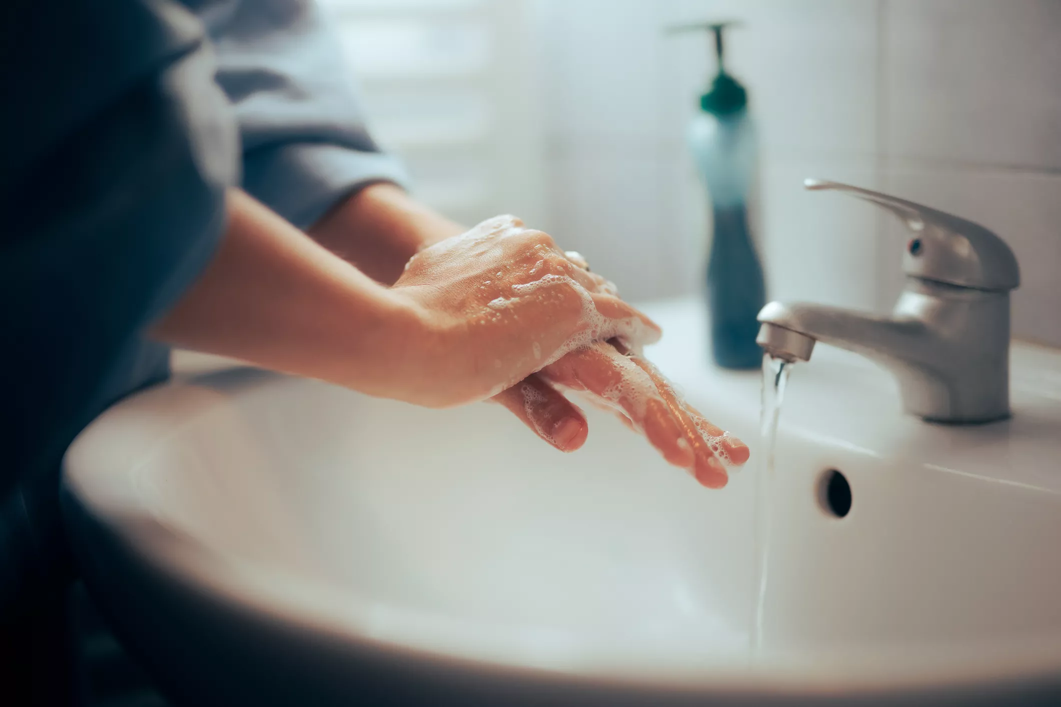Käsienpesu. Henkilö pesee käsiä saippualla hanan alla.