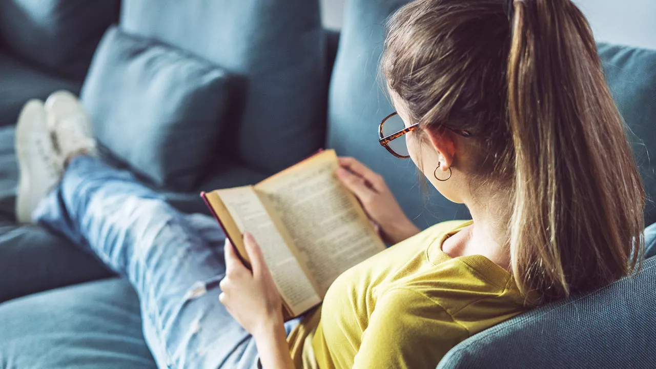 Nainen lukee kirjaa sohvalla