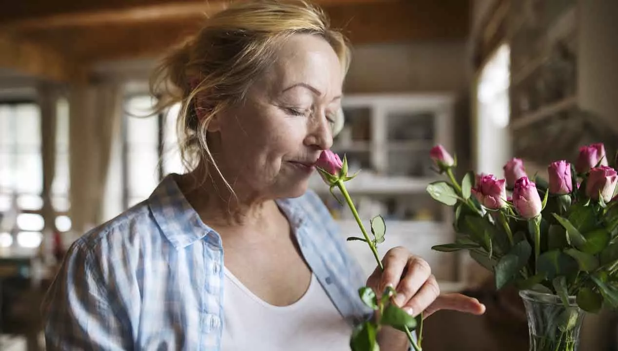 Parkinsonin taudin oireet. Nainen haistaa kukkaa.
