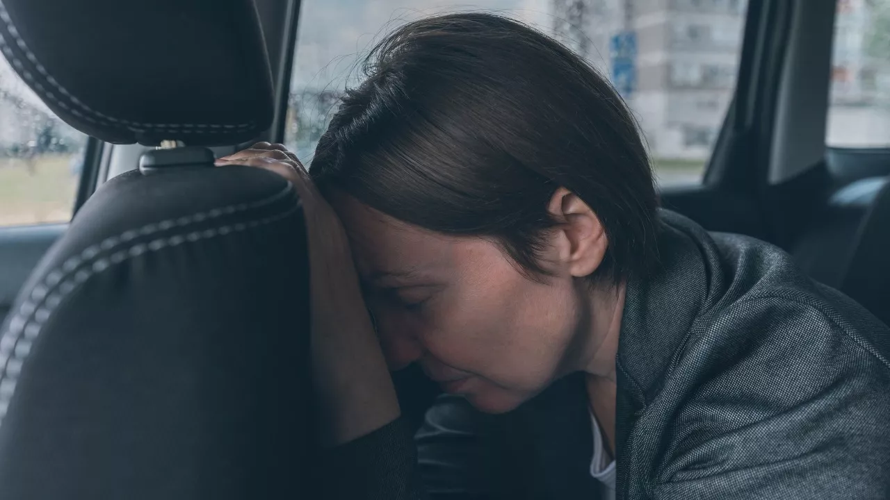 Burnout oireet ovat moninaiset: Kuvassa nainen nojaa uupuneena päätään auton takapenkillä etupenkin takaosaa.