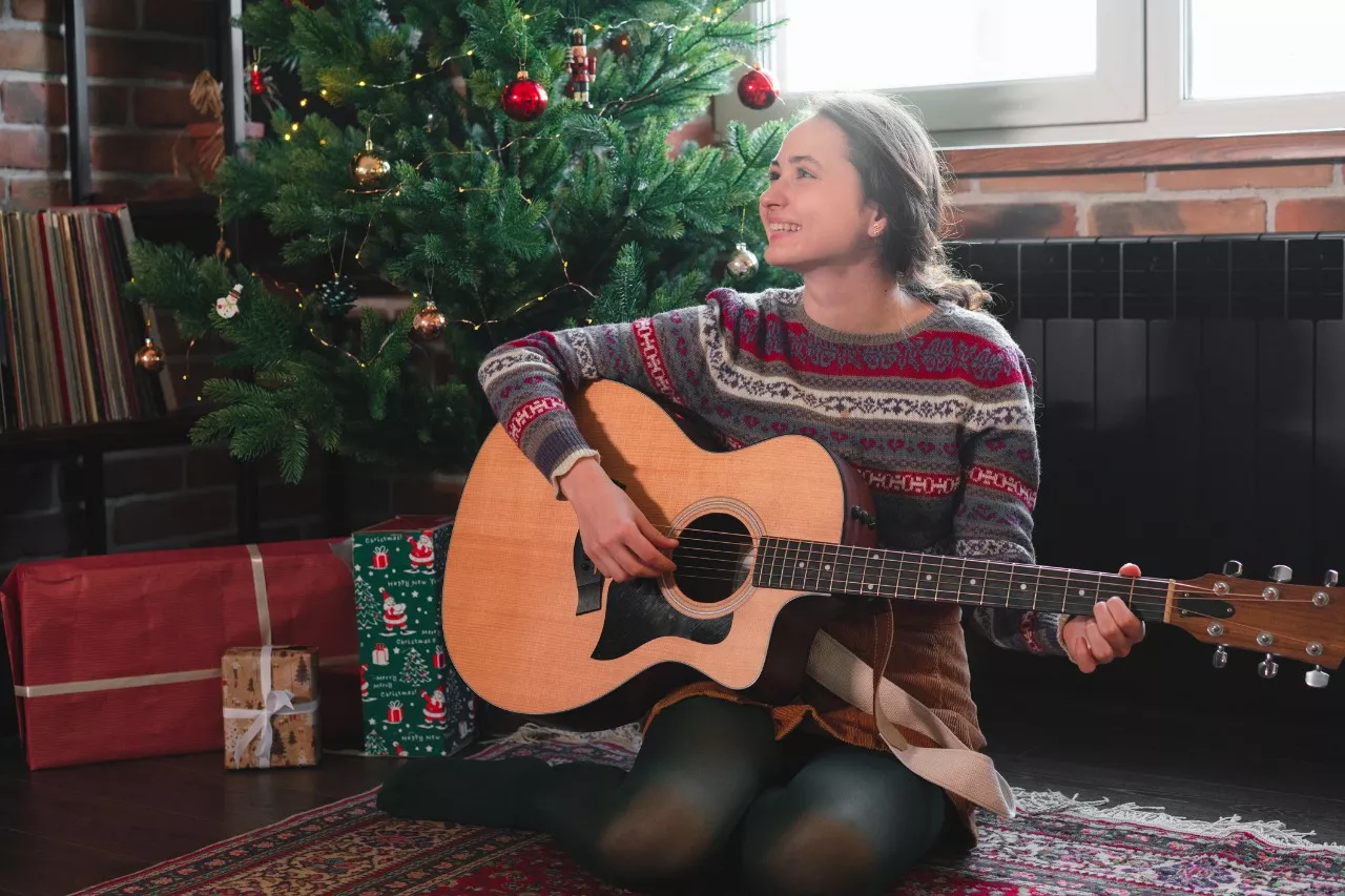 Nainen soittaa kitaraa joulukuusen vieressä