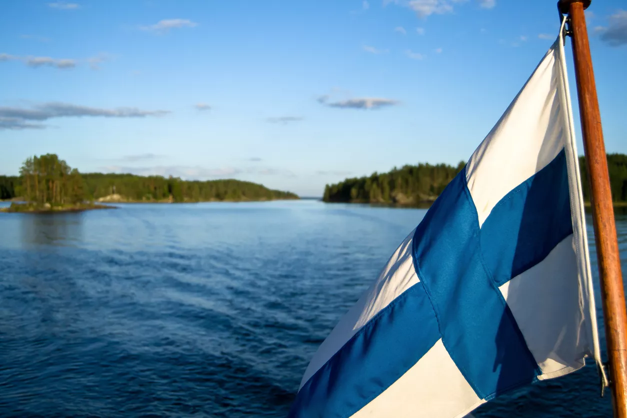 Suomen lippu liehuu järvimaisemassa.