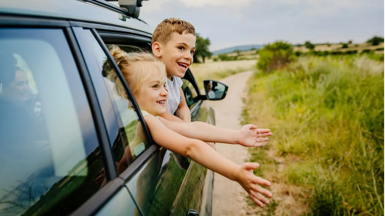 kaksi lasta kurkottaa ulos auton ikkunasta