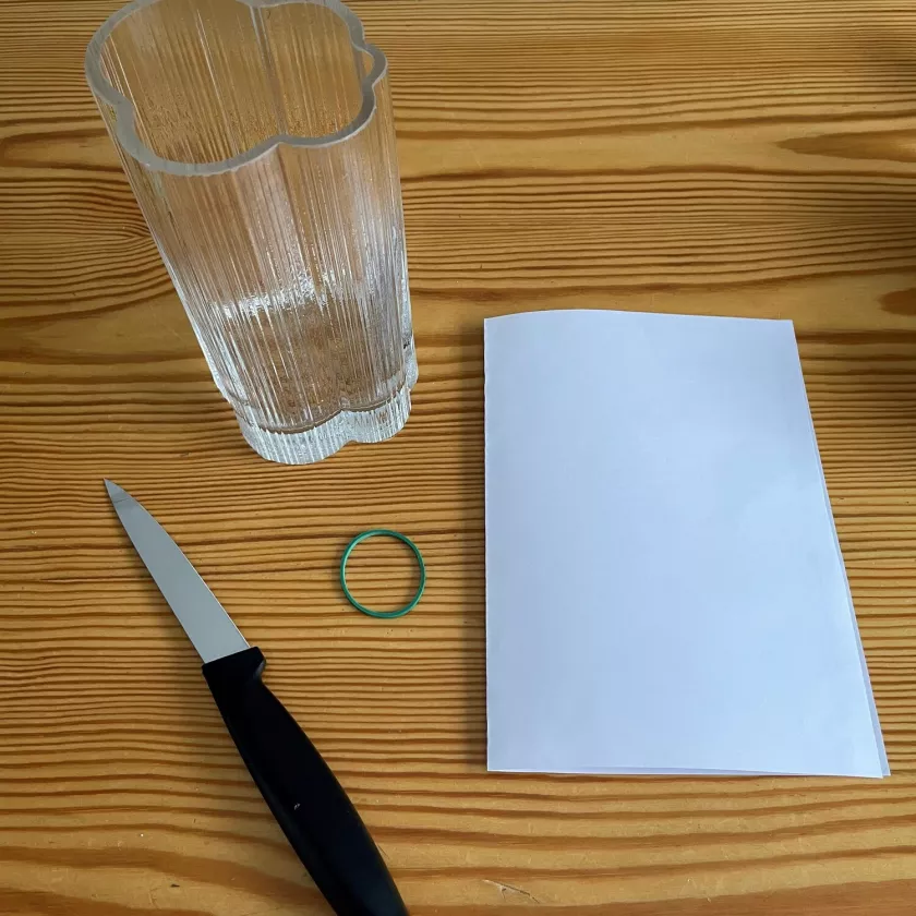 Maljakko, valkoinen paperi, kuminauha ja veitsi pöydällä.