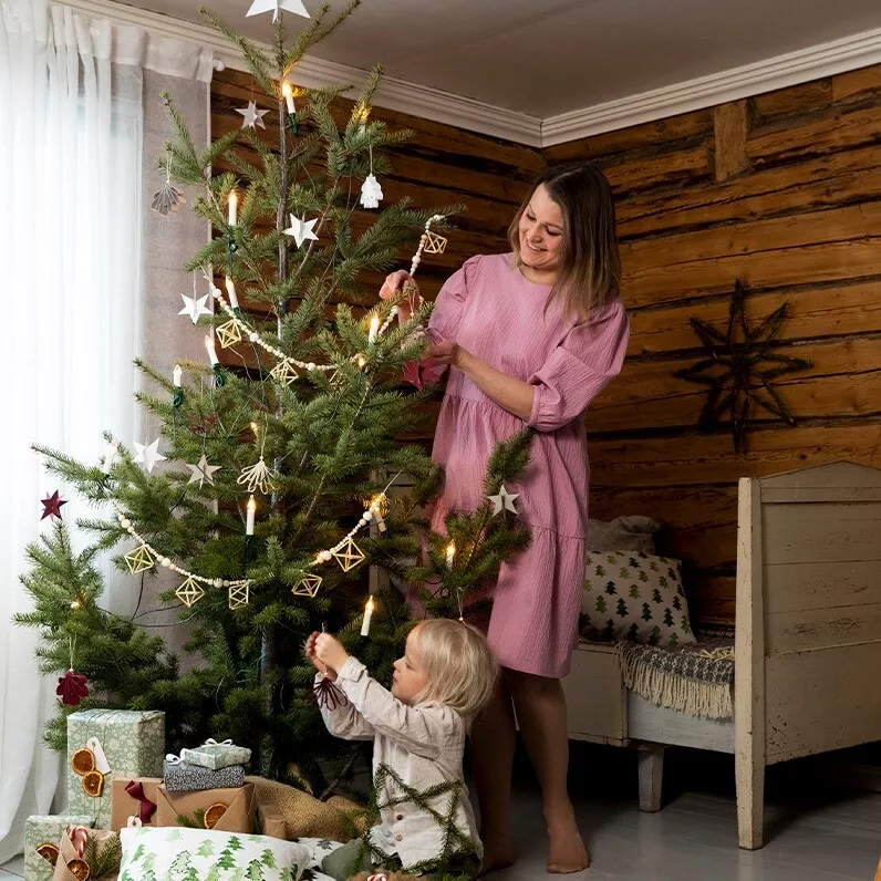 Nainen ja lapsi ripustavat kartongista tehtyjä tähtikoristeita joulukuuseen.