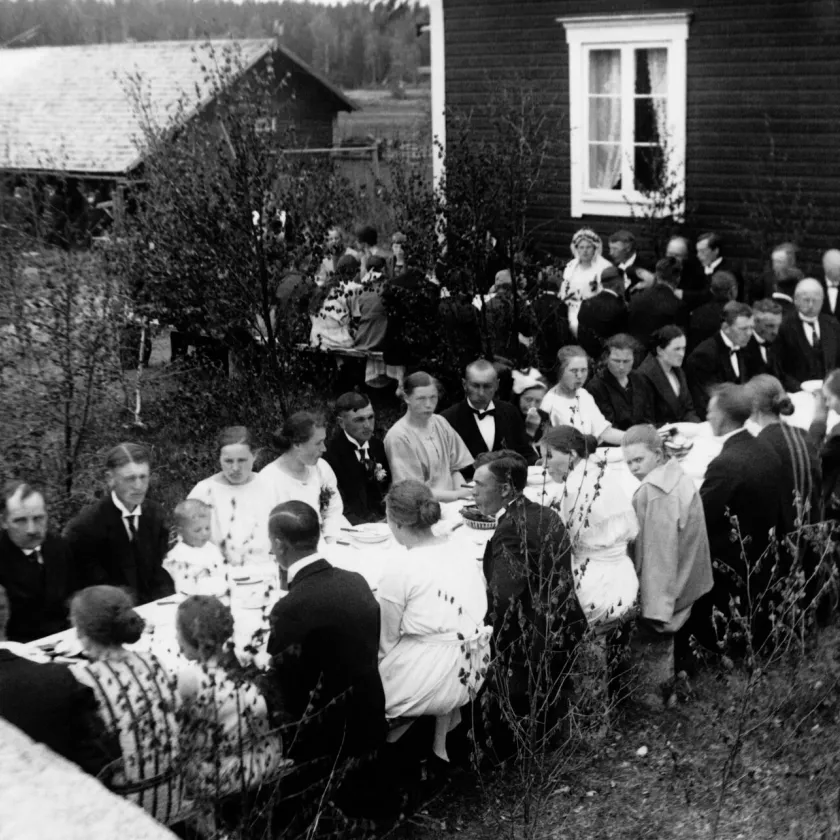 Maalaishäissä 1930-luvulla juhlavieraat istuvat pihamaalla pitkien pöytien ääressä.