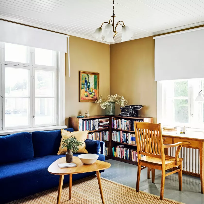 Majoitushuoneessa on sohva ja sohvapöytä, kirjoituspöytä ja tuoli sekä kirjahylly kirjoineen.