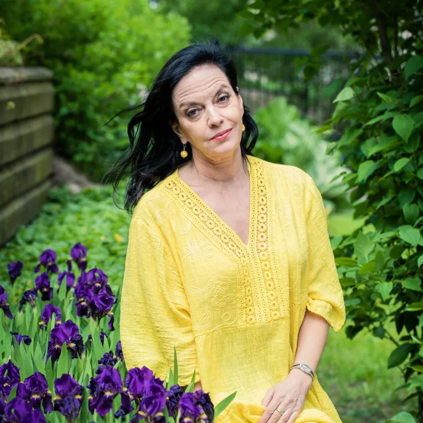 Anna-Leena Härkönen istuu omassa puutarhassaan kirkkaan keltainen mekko yllään. 