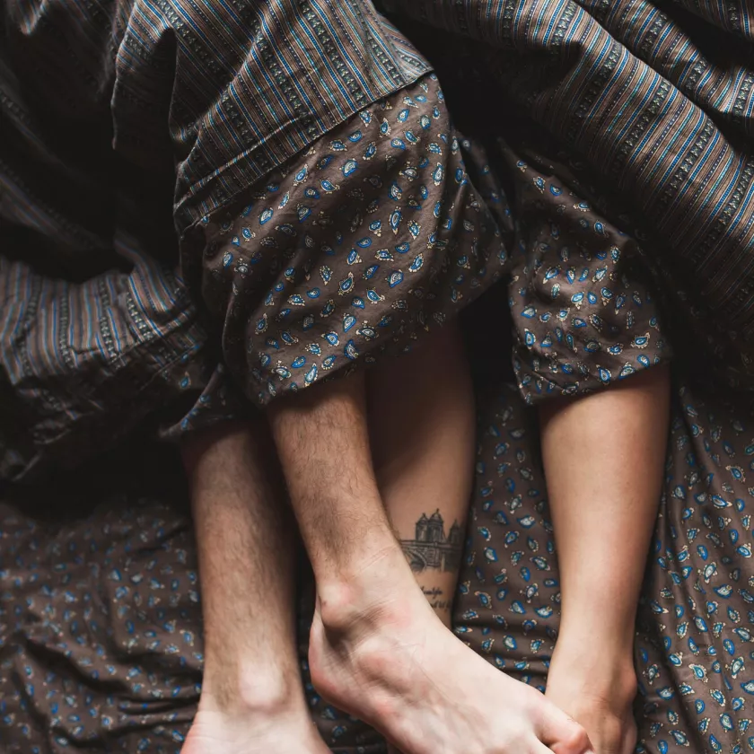Miehen ja naisen jalat näkyvät peiton alta.