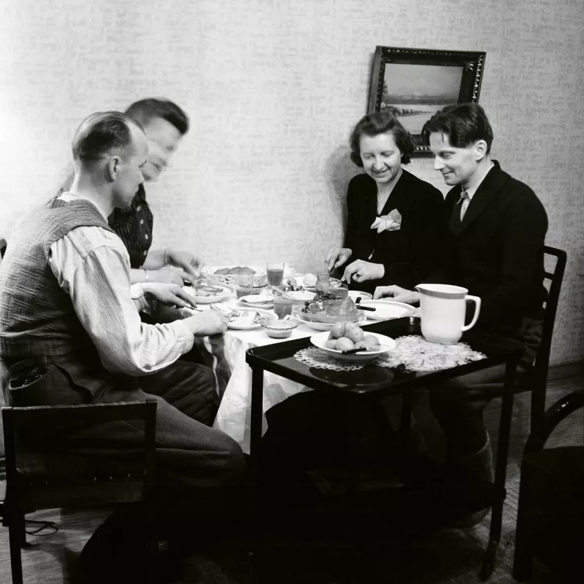 Kokokuva neljästä ihmisestä syömässä ruokapöydän ääressä.