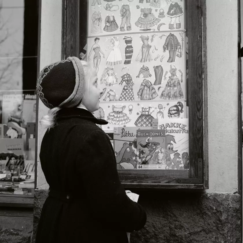Paperikaupan ikkunaan ripustetut paperinuket kiinnittävät pikkutytön huomion 1950-luvulla.