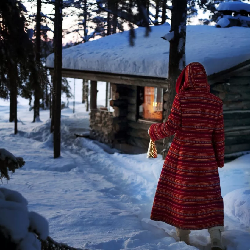 Nainen kävelemässä lumista polkua pitkin joulusaunaan.