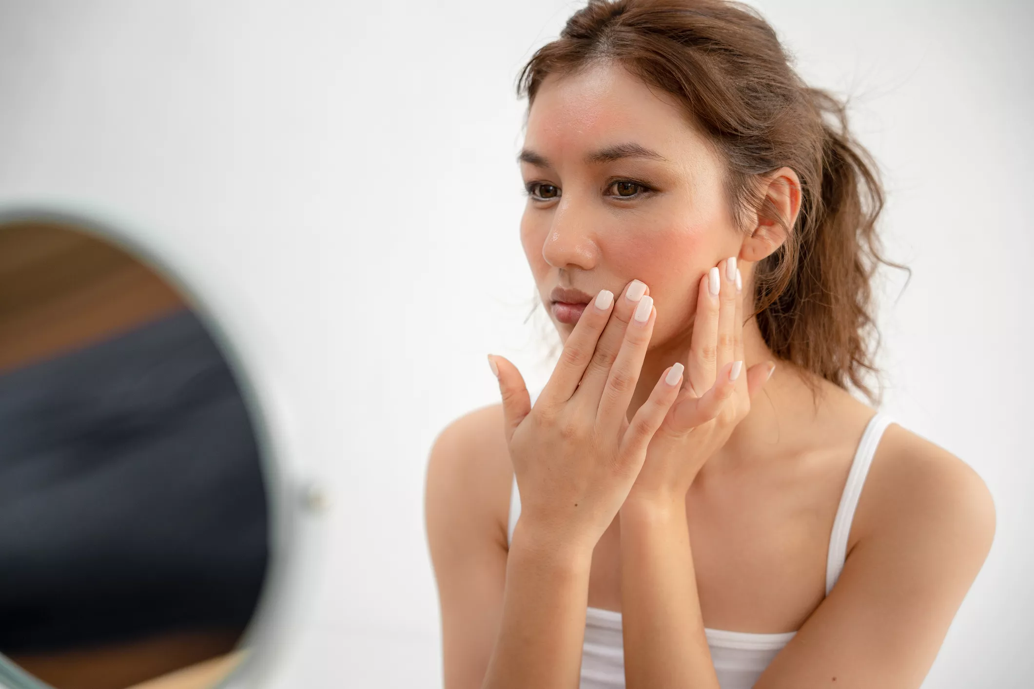 Kosmetiikka-allergia. Nainen koskettelee peilin edessä punoittavia kasvojaan.