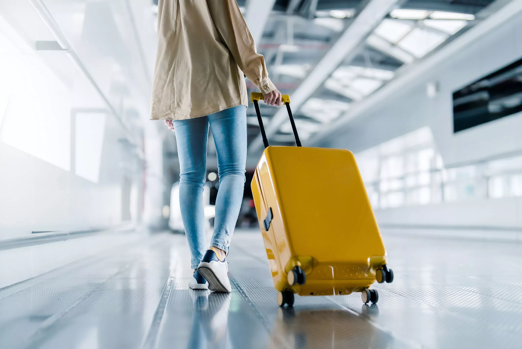 Nainen vetää keltaista matkalaukkua lentokentällä.