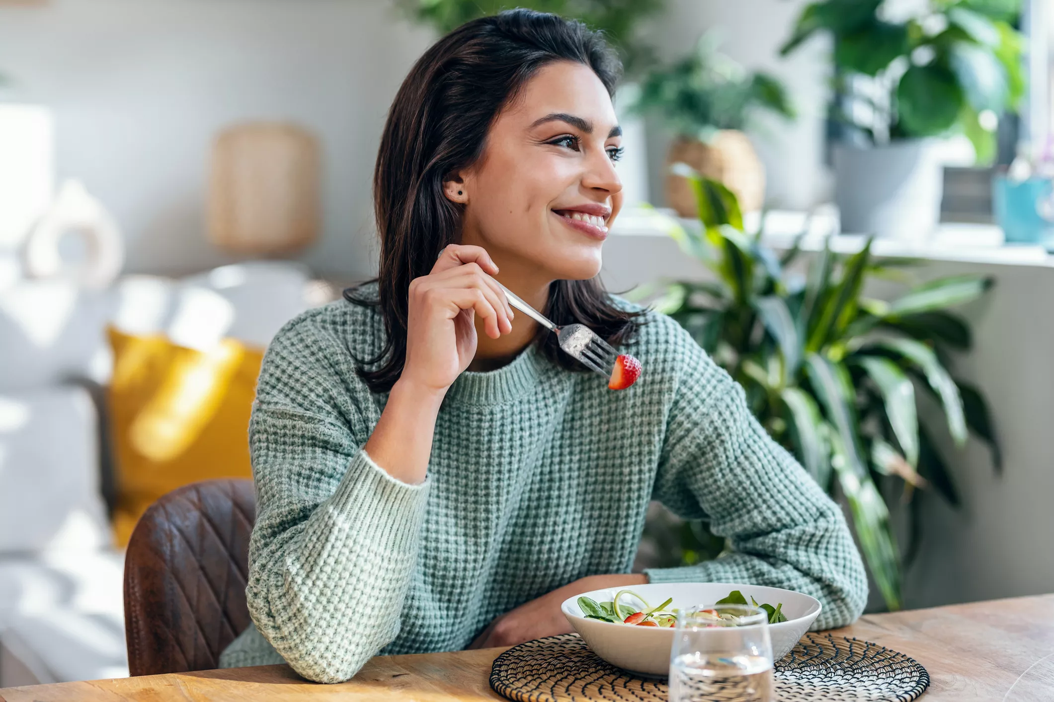 Auttavatko vitamiinit väsymykseen? Hymyilevä nainen syö salaattia kotona.