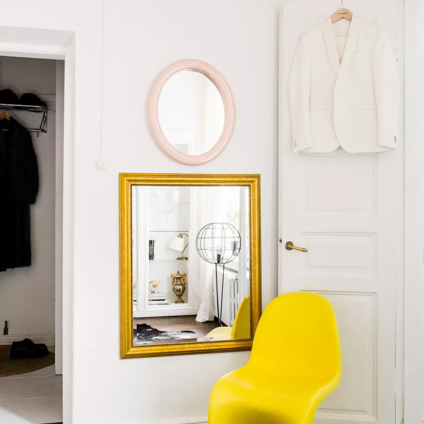Vitran keltainen tuoli oven edessä makuuhuoneessa. Seinällä on pyöreä peili (yllä) ja kultarkehyksinen peili (alla).