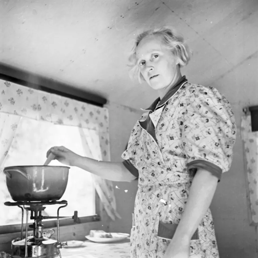 Nainen valmistaa ruokaa retkikeittimellä kesämajassa.