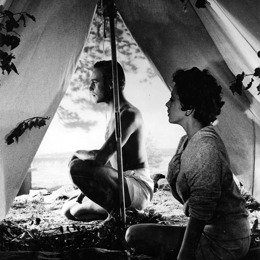 Nainen istuu teltassa, mies teltan oviaukossa.