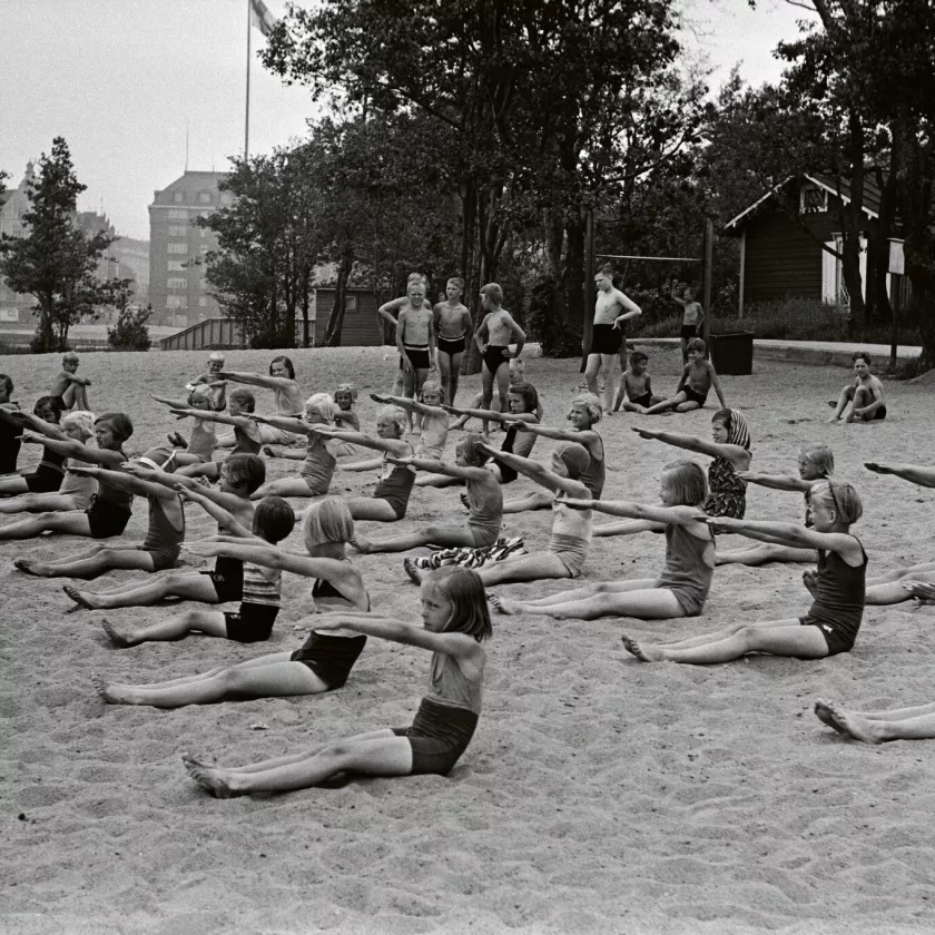 Lapset istuvat hiekalla harjoittelemassa uintiliikkeitä.