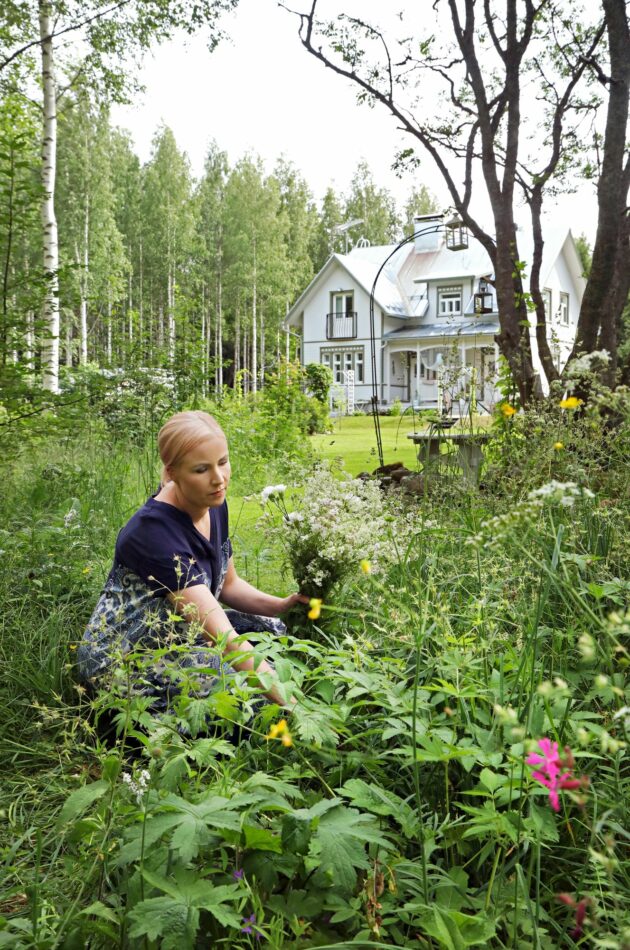 Tarja kerää kukkia niityltä. Hänen perheensä koti näkyy taustalla. 