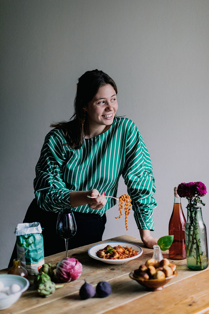 Ruokakirjailija Tara Junker syö pastaa seisaaltaan pöydän ääressä.