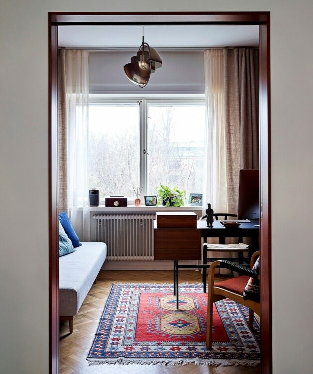 11. Koristeellinen matto tuo pieneen huoneeseen syvyyttä. Sininen ja punainen toistuvat sohvatyynyissä ja nojatuolin verhoilussa.