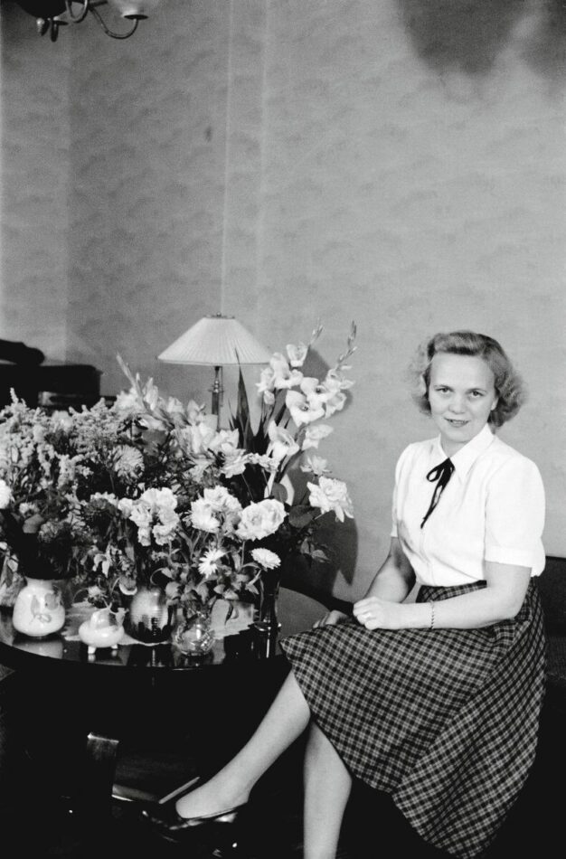 Nainen istuu kukkakimppujen vieressä.