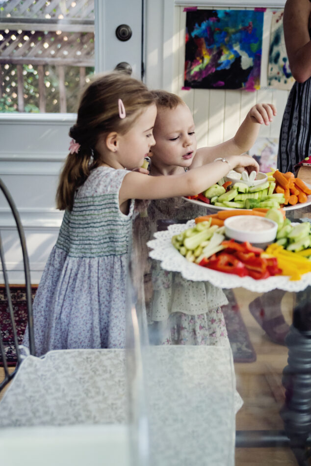 Kaksi lasta ottaa kasviksia lautaselta.